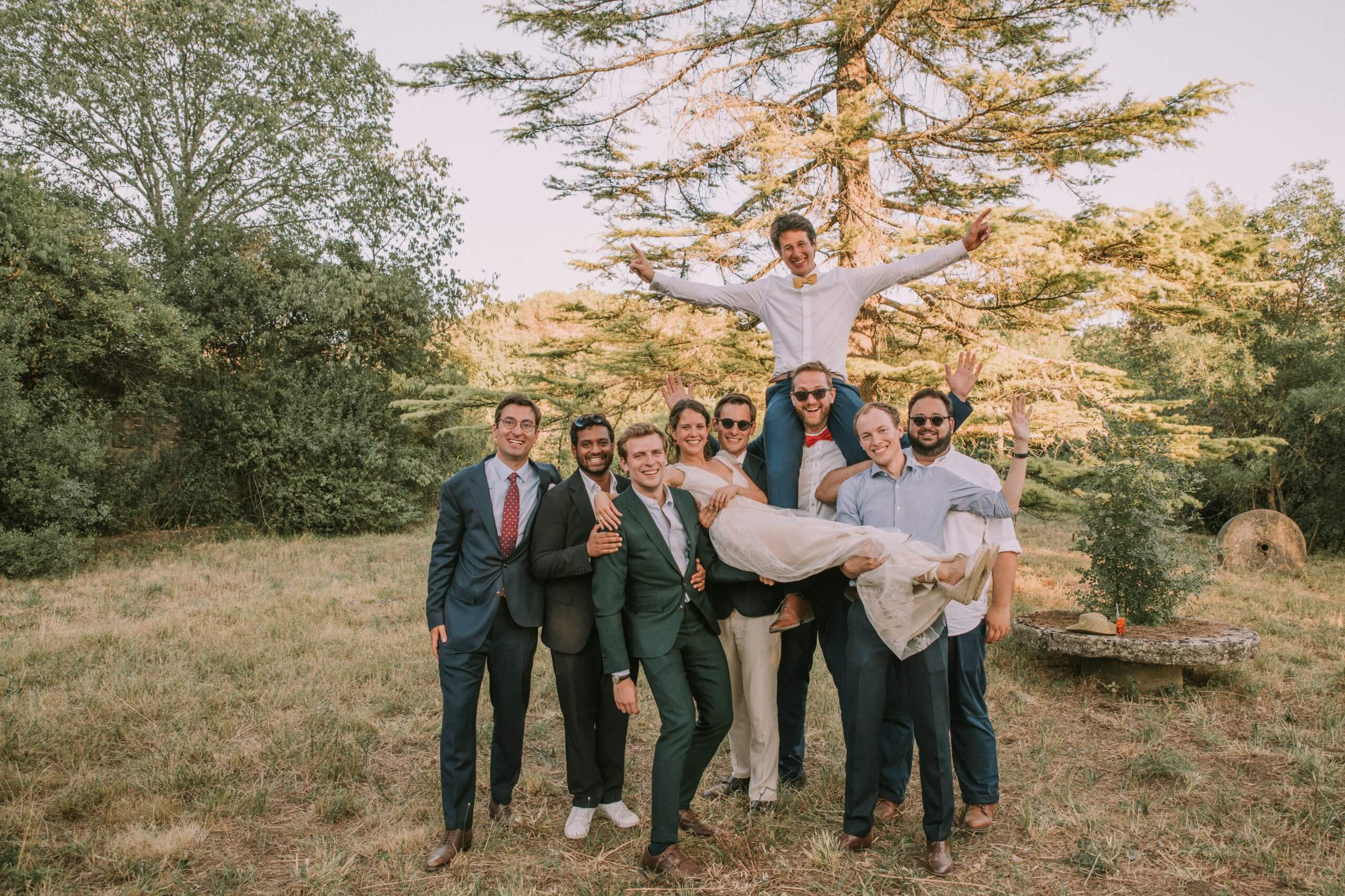 Photo de groupe fun avec les mariés Mariés portés par leurs amis lors d’une photo de groupe en extérieur